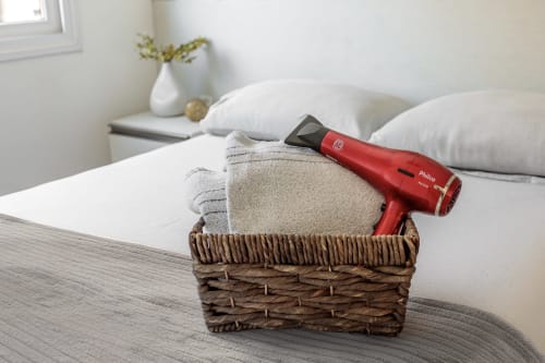 Cesta de vime com toalhas dobradas e secador de cabelo vermelho na cama do apartamento à beira-mar em Florianópolis