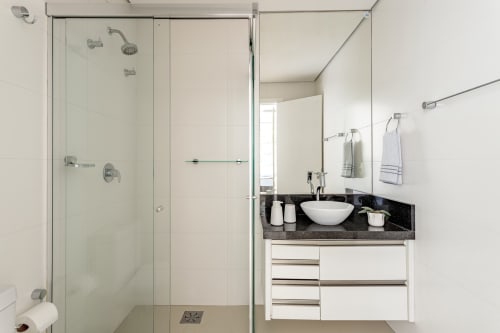 Banheiro moderno no apartamento Villa Dell'Acqua, Canasvieiras, Florianópolis com chuveiro de vidro, cuba branca e acabamento escuro