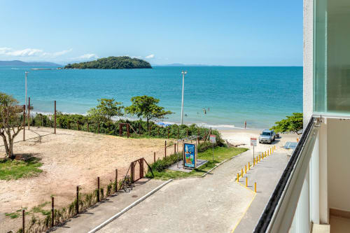 Vista da praia do apartamento Villa Dell'Acqua em Canasvieiras, Florianópolis, com areia, oceano turquesa e ilha