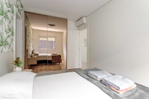 Quarto moderno com guarda-roupa espelhado, vista para o mar e toalhas dobradas na Sua Estadia SC, Canasvieiras, Florianópolis