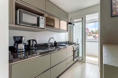 Cozinha moderna com bancada em granito escuro, eletrodomésticos em aço inoxidável e portas de vidro com vista para o mar