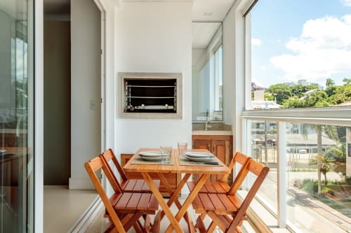 Sala de jantar com mesa e cadeiras de madeira com vista para a praia de Canasvieiras em apartamento villa em Florianópolis
