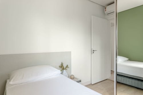 Quarto moderno no apartamento Villa Dell'Acqua em Canasvieiras, Florianópolis com cama branca, decoração minimalista e toque verde