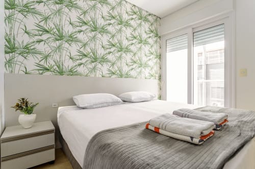 Quarto moderno na Villa Dell'Acqua em Florianópolis com papel de parede botânico, roupas de cama brancas e vista para o mar da varanda