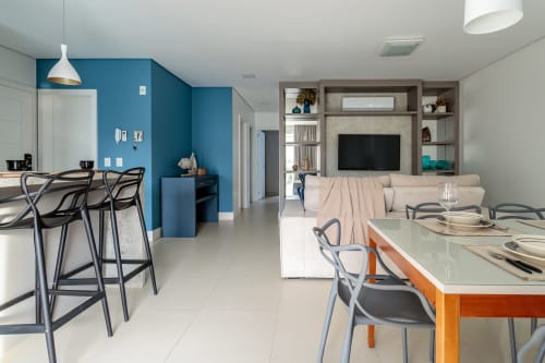 Apartamento moderno e integrado em Florianópolis com parede em azul, ilha na cozinha, área de refeições e sala de estar com TV