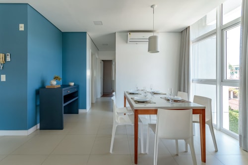 Sala de jantar de apartamento à beira-mar moderno com parede de destaque azul, mesa de madeira, cadeiras brancas e vista para o mar em Canasvieiras