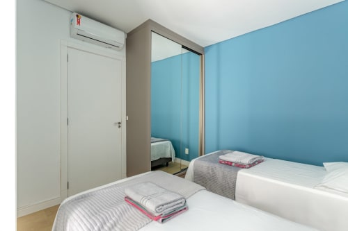 Quarto moderno com duas camas de solteiro, parede de destaque em turquesa, guarda-roupa espelhado e ar-condicionado no apartamento de Canasvieiras