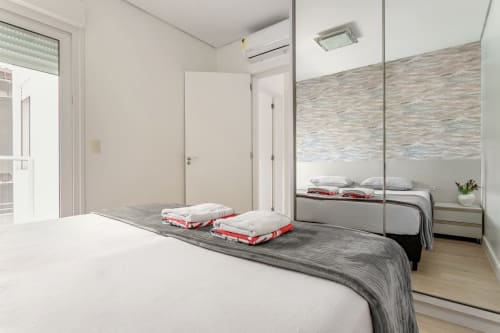 Quarto de apartamento moderno à beira-mar em Florianópolis com guarda-roupa espelhado, vista para o mar e móveis contemporâneos