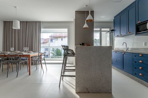 Cozinha integrada moderna com armários azuis, ilha cinza e vista para o mar em apartamento em Florianópolis