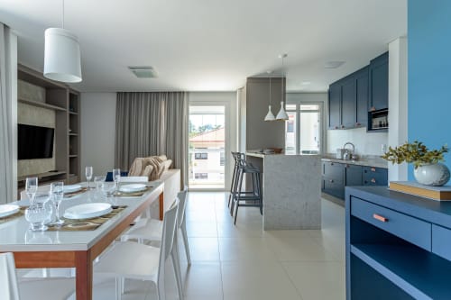 Cozinha e sala de jantar modernas em apartamento à beira-mar, Florianópolis, com armários azuis, eletrodomésticos em aço inoxidável