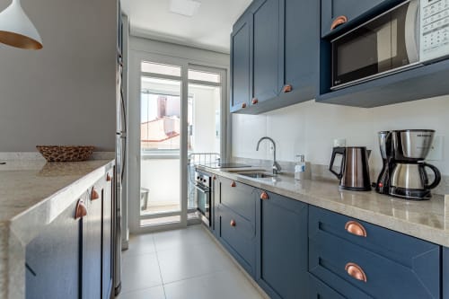 Cozinha moderna com armários azul escuro, eletrodomésticos em aço inoxidável e vista para o mar em Canasvieiras, Florianópolis