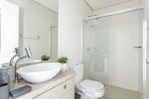 Banheiro moderno no apartamento Villa Dell'Acqua, Florianópolis com cuba redonda, chuveiro de vidro, sanitário e acesso à praia.