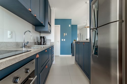 Cozinha moderna com armários azul marinho, eletrodomésticos em aço inoxidável e bancadas de granito em apartamento à beira-mar