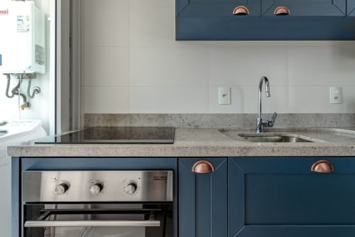 Cozinha moderna com bancada cinza, forno em aço inoxidável, torneira cromada e armários azul-escuro em apartamento à beira-mar