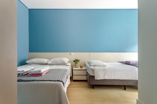 Dois leitos com roupa de cama branca em apartamento moderno em Canasvieiras com parede de destaque azul turquesa e piso de madeira