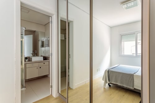 Quarto moderno com guarda-roupa de portas espelho, piso de madeira e janela em Canasvieiras, Florianópolis