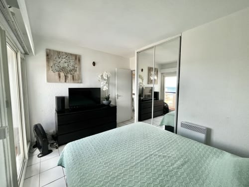 Chambre lumineuse de l'appartement Barcaresa, Port Leucate, avec vue mer, literie menthe, commode noire, TV, armoire miroir