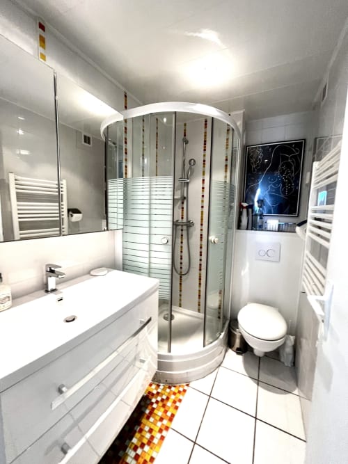 Salle de bain moderne à l'appartement Barcaresa de Port-Leucate avec douche en verre courbe, vasque blanche, toilettes et carrelage coloré
