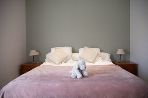 Chambre élégante du Domaine de Castagnère avec édredon violet, oreillers crème, tables de nuit en bois et peluche bleue.