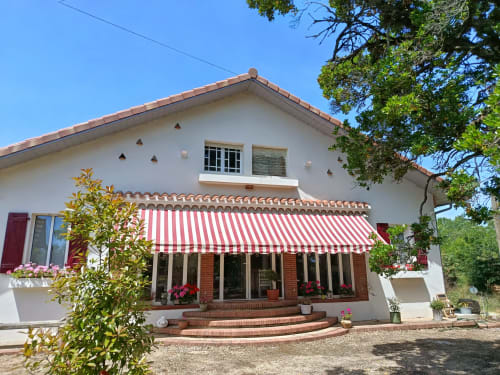 Domaine de Castagnère, gîte de charme avec façade blanche, store rayé rouge, patio en brique et fleurs roses