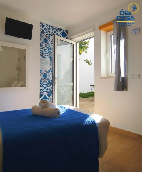 Quarto luminoso na Casa das 7 Janelas, Peniche com cama azul, azulejos portugueses e acesso ao pátio