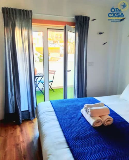 Quarto luminoso da Casa das 7 Janelas Peniche com roupa de cama azul, toalhas enroladas e porta para pátio do jardim