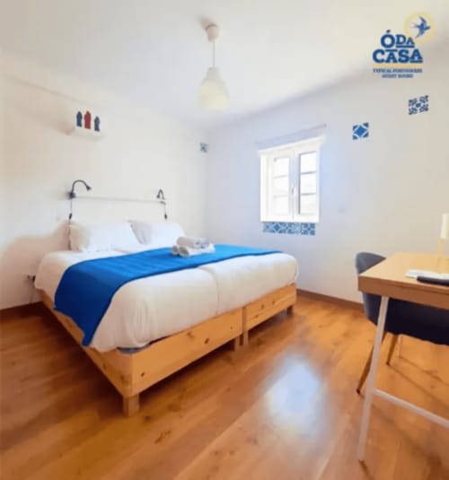 Quarto luminoso na pousada Casa das 7 Janelas em Peniche com cama de madeira, roupa de cama azul e paredes brancas