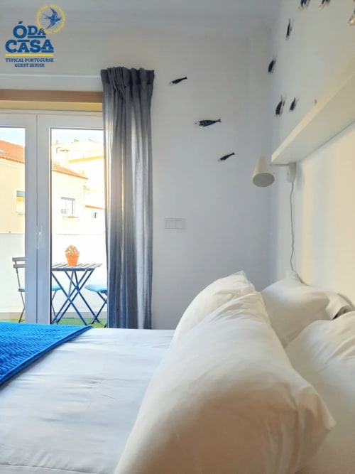 Quarto luminoso na Casa das 7 Janelas em Peniche com roupa de cama branca, decoração temática marinha e vista para varanda