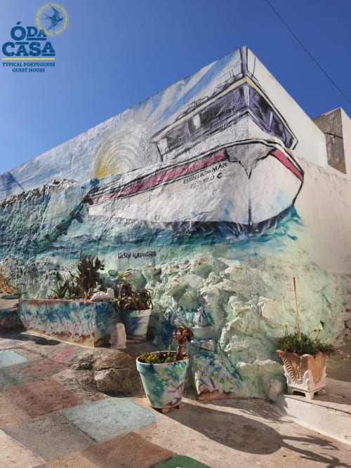 Mural colorido na fachada branca da hospedaria Ó da Casa em Peniche, Portugal, com floreiras decorativas abaixo