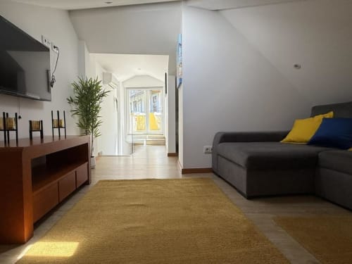 Bright Chaves B&B living room with gray sofa, wooden furniture, potted plant, and natural light from arched doorway