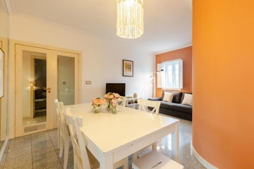 Bright dining and living area in Chaves B&B with white table, orange accent wall, and modern furnishings