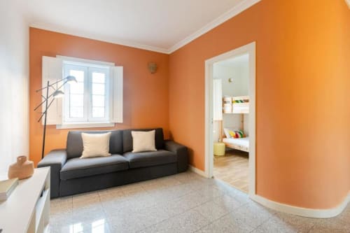 Bright orange living room with black sofa, window, and doorway to bedroom in Chaves B&B