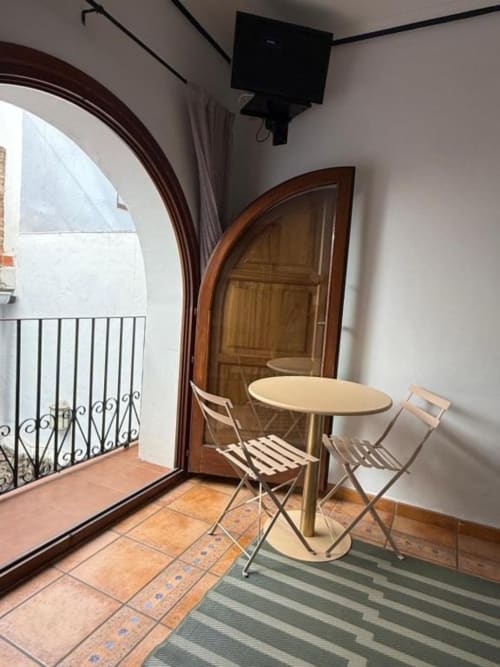 Zona de asientos en balcón del Hotelito Oliva Pensión en Oliva con mesa redonda, sillas y puerta de madera arqueada