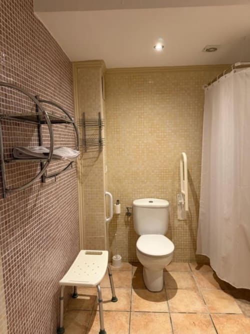 Baño accesible en Hotelito Oliva Pensión con inodoro blanco, zona de ducha, barras de apoyo y dispositivos de movilidad en Oliva, España