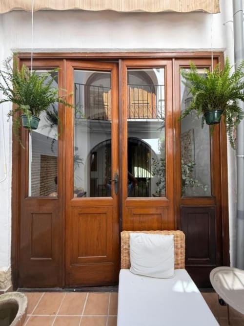 Puertas francesas de madera con cristales que se abren al patio del Hotelito Oliva Pensión en Oliva, España, decoradas con adornos colgantes