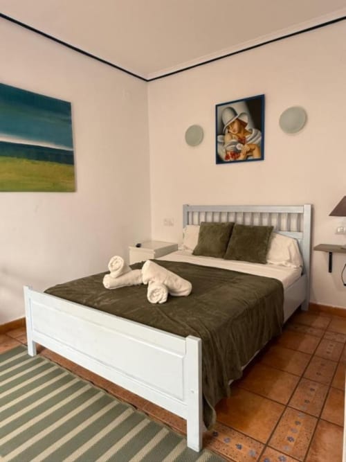 Amplia habitación de hotel en Hotelito Oliva Pensión en Oliva con cama blanca, ropa de cama oscura, decoraciones de toallas y estilo moderno