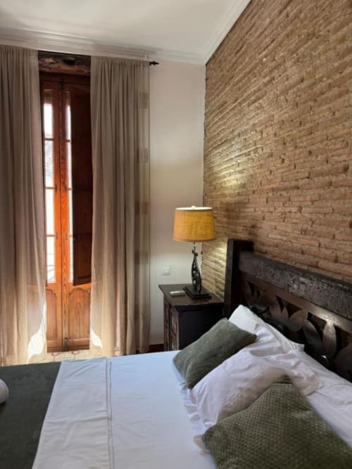 Habitación moderna en Hotelito Oliva con pared de ladrillo visto, puertas de madera, lámpara y cama con sábanas blancas y almohadas verdes