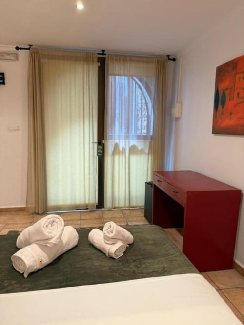Habitación moderna en Hotelito Oliva con toallas enrolladas en la cama, escritorio rojo, puertas de cristal al balcón y cortinas con vista a la ciudad