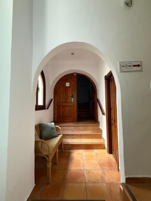 Pasillo abovedado con suelo de baldosa terracota en Hotelito Oliva Pensión en Oliva, España, con puertas de madera y zona de estar