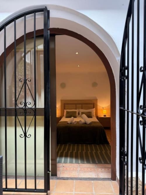 Elegante entrada arqueada con puertas de hierro negro ornamentales que abren a una habitación del Hotelito Oliva Pensión en Oliva, España