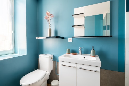 Salle de bain moderne à la Maison d'hôtes Dupain & Dubeurre à Limoges : murs turquoise, vasque blanche, toilettes et miroir.
