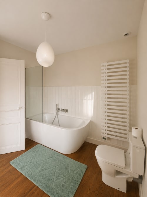 Salle de bain moderne à la Villa Eliane Étretat avec baignoire blanche, toilettes, sèche-serviettes chauffant, parquet et tapis vert