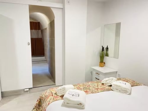 Quarto luminoso na Casa das 7 Janelas em Peniche com roupa de cama floral, toalhas brancas, espelho e acesso à casa de banho privada