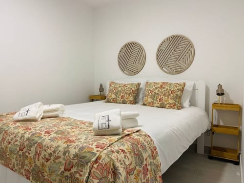 Quarto luminoso na Casa das 7 Janelas em Peniche com duas camas, roupa de cama com padrão floral, pratos decorativos na parede e detalhes de madeira