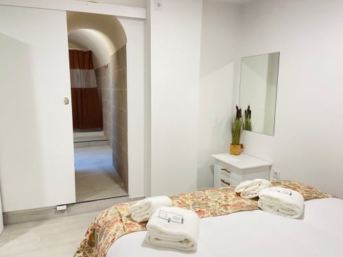 Quarto luminoso na Casa das 7 Janelas em Peniche com roupa de cama floral, toalhas brancas, espelho e casa de banho privativa
