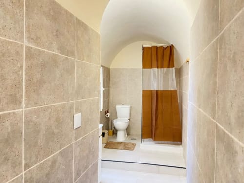 Casa das 7 Janelas em Peniche: banheiro moderno com azulejos bege, teto branco, vaso sanitário e cortina marrom no chuveiro