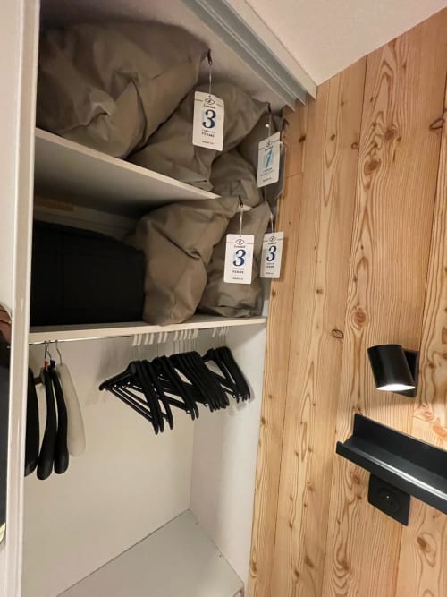 Placard de l'appartement GNM à Vars avec housses de vêtements étiquetées, cintres noirs et meubles en bois