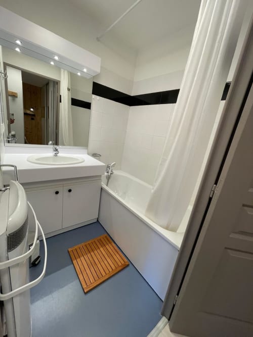 Salle de bain moderne de l'appartement 303 GNM à Vars avec équipements blancs, carrelage mural et tapis de bain en bois