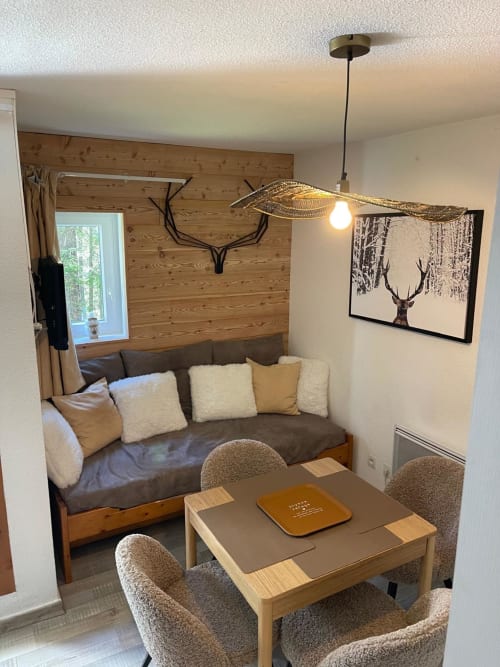 Studio cosy à GNM Vars avec murs en bois, canapé gris, table à manger, luminaire suspendu et décoration de cerfs