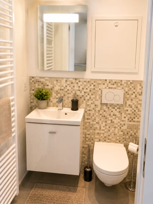 Salle de bains moderne avec toilettes murales, vasque blanche, dosseret en mosaïque et miroir dans l'appartement Mattbnb